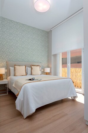 Ein Schlafzimmer mit einem großen Bett, zwei Nachttischen, einem Fenster mit Blick und ornamental gestalteter Tapete.