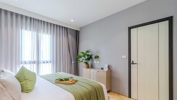 A modern bedroom with a bed, green and white pillows, a bedside table with a plant, and a wardrobe. - The Title Legendary Bang-Tao  (Choeng Thale)