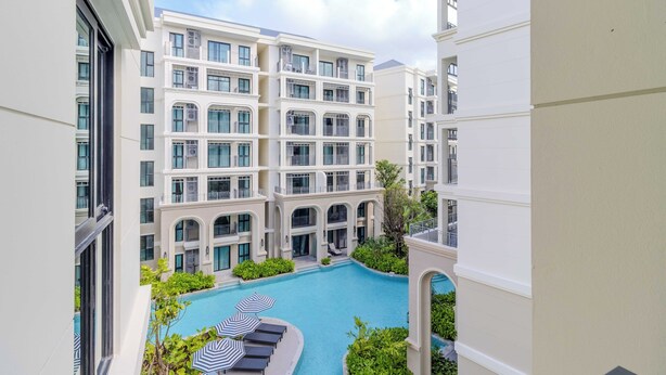 Un hôtel à plusieurs étages doté d’une cour intérieure comprenant une piscine, des chaises longues et des parasols.