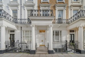 A building facade with a central entrance flanked by columns, a gated entrance, and a bicycle parked outside. - Devonshire Terrace - 2 Bedroom Apartment (London)