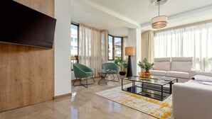 A modern living room with a flat-screen TV, two green armchairs, a white sofa, a glass coffee table, and a lamp. - Luxury Apartment in City Center Puerta Real II (Granada)