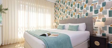A modern bedroom with a large bed, a nightstand with a lamp, and a geometric-patterned wall.