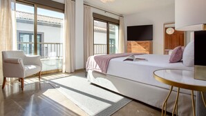 A modern hotel room with a large bed, a sitting area, a television, and a balcony with a view. - Luxury Apartment in City Center Puerta Real II (Granada)