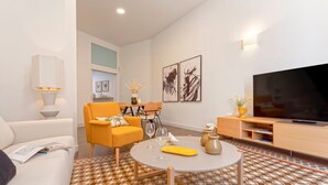 Ein modernes Wohnzimmer mit Sofa, gelbem Sessel, rundem Couchtisch und Flachbildfernseher.