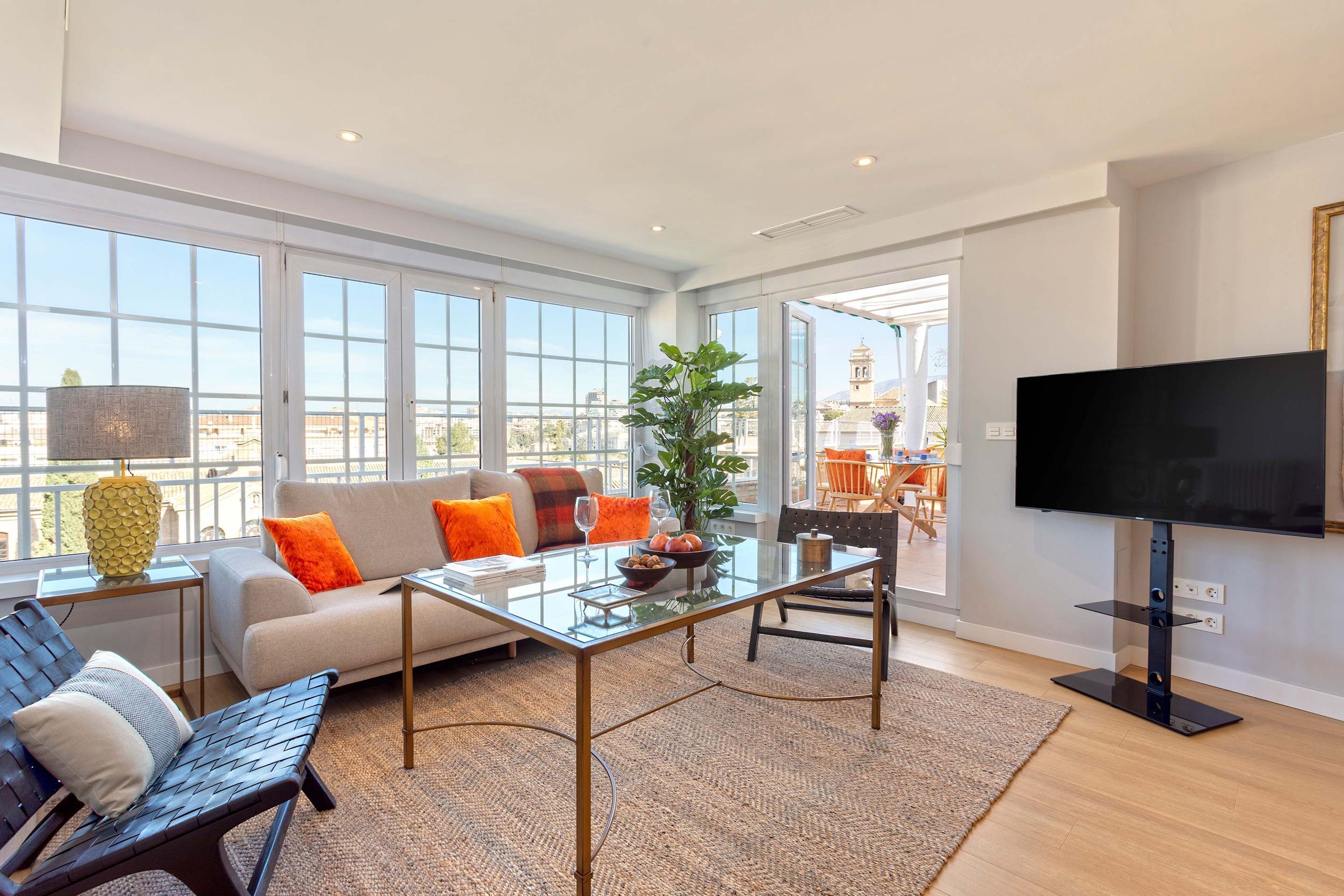 A modern living room with a glass coffee table, sofa, and a flat-screen TV.