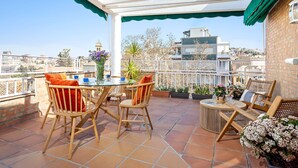 Una terrazza con tavolo e sedie, piante in vaso e vista sulla città.
