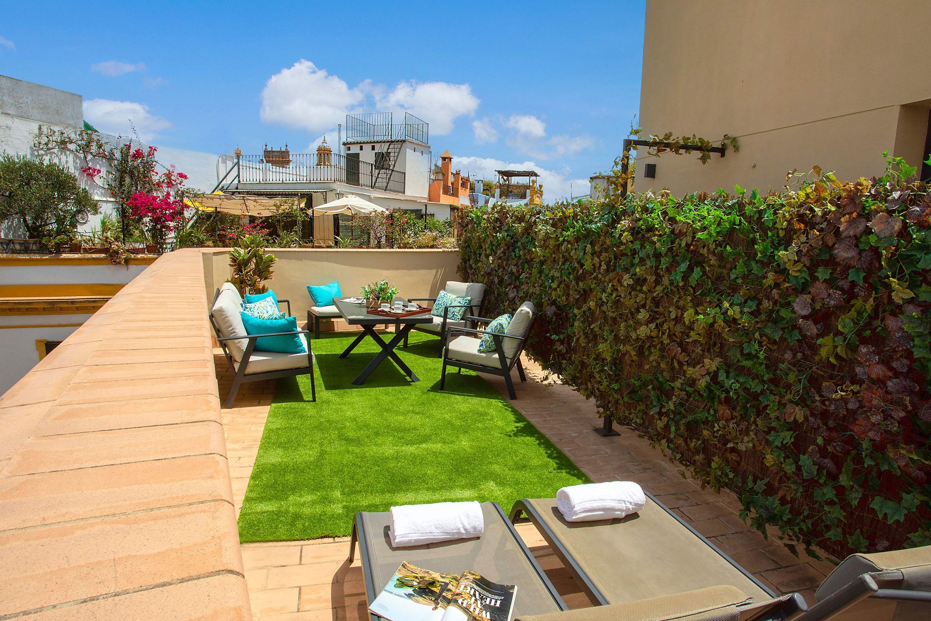 A rooftop terrace with a green lawn, lounge chairs, and a table.