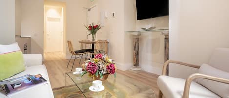 A modern living room with a glass coffee table, a sofa, a wicker chair, and a TV mounted on the wall.