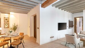 A modern living room with a dining area, featuring a round table, chairs, a flat-screen TV mounted on the wall, and a sofa. - Exclusive Apartment in Granada Center Horno Marina 2 (Granada)