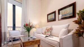 A living room with a sofa, a wooden coffee table, a chair, a vase with flowers, and two framed pictures on the wall. - Exclusive Apartment Near Cathedral Rodrigo Caro IV (Seville)