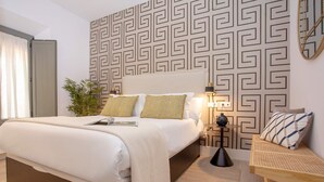 Een moderne hotelkamer met een groot bed, een nachtkastje met lamp, een klein bijzettafeltje en een decoratief wandpaneel.