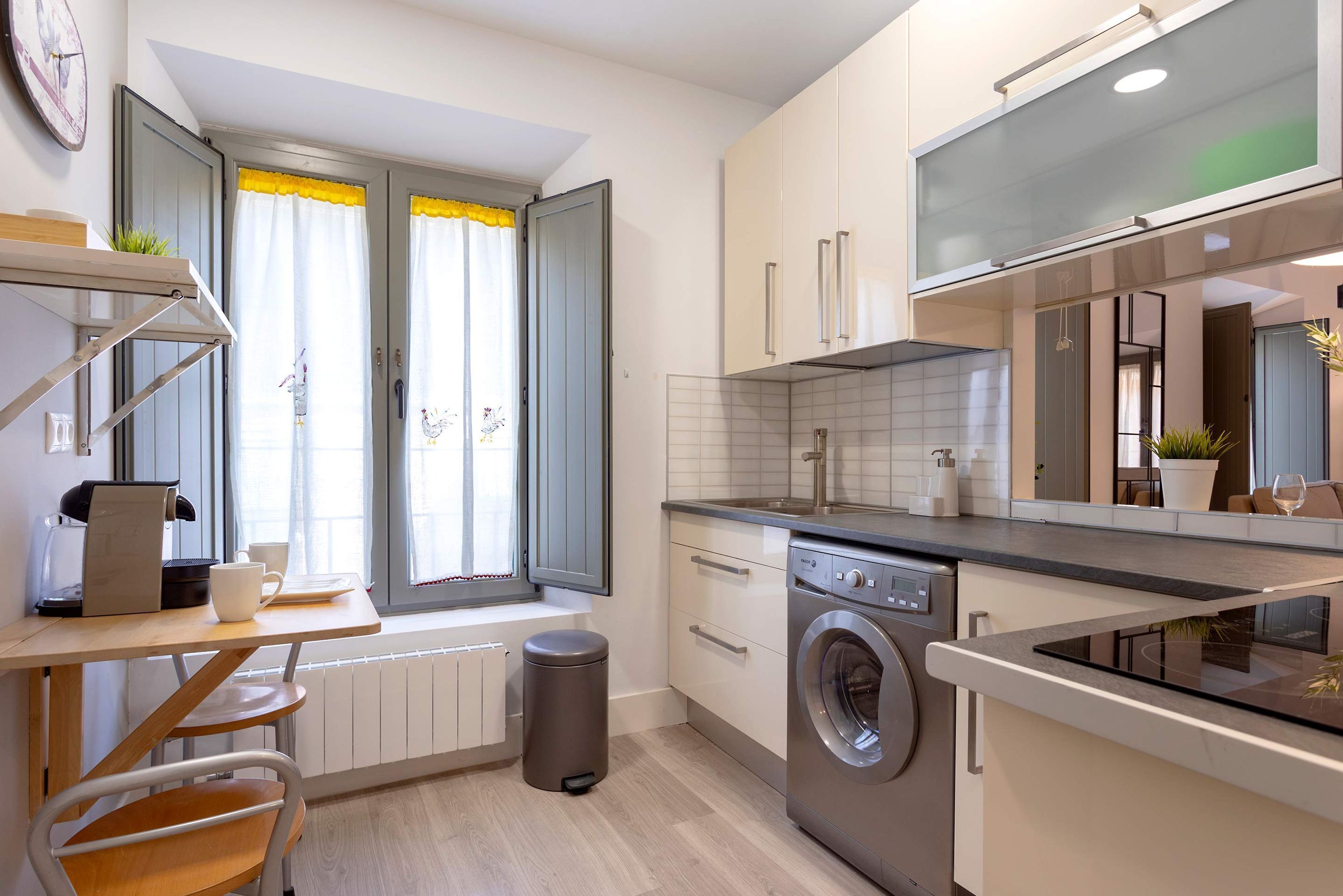 Une cuisine moderne équipée d’un lave-linge encastré, d’une fenêtre avec des rideaux et d’un plan de travail sur lequel se trouve une machine à café.