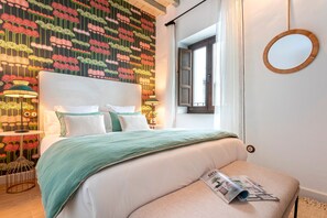 A neatly made bed with a green blanket, a bedside table with a lamp, and a wall with a floral pattern. - Luxury Duplex in Granada Horno Marina 5 (Granada)