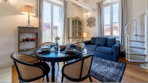 A dining area with a round table, chairs, and a lamp. There is a sofa and a staircase in the background. - Luxury Apartment in Florencia Scarlatti (Florence)