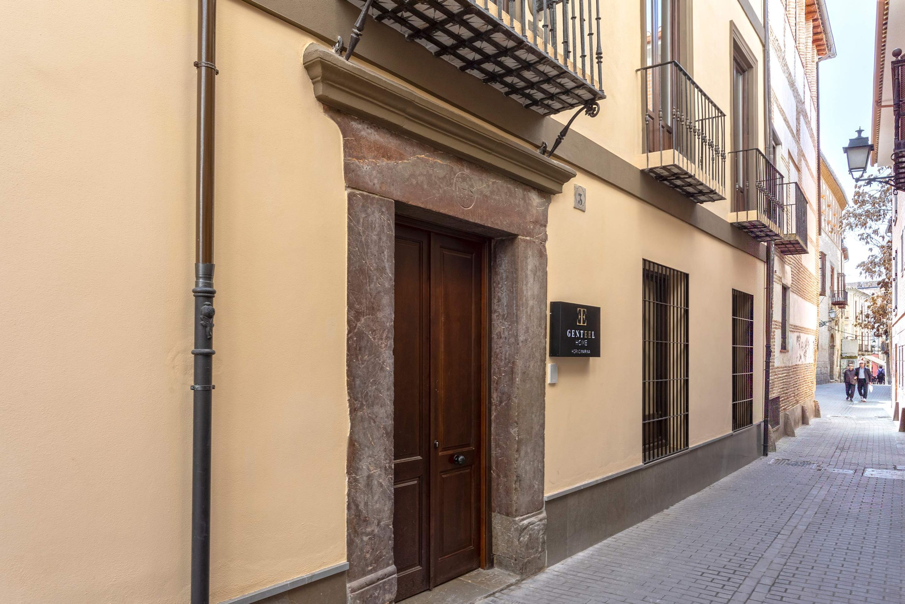 Un edificio con una porta in legno, un cartello con la scritta “GENTELLE” e un marciapiede in piastrelle.