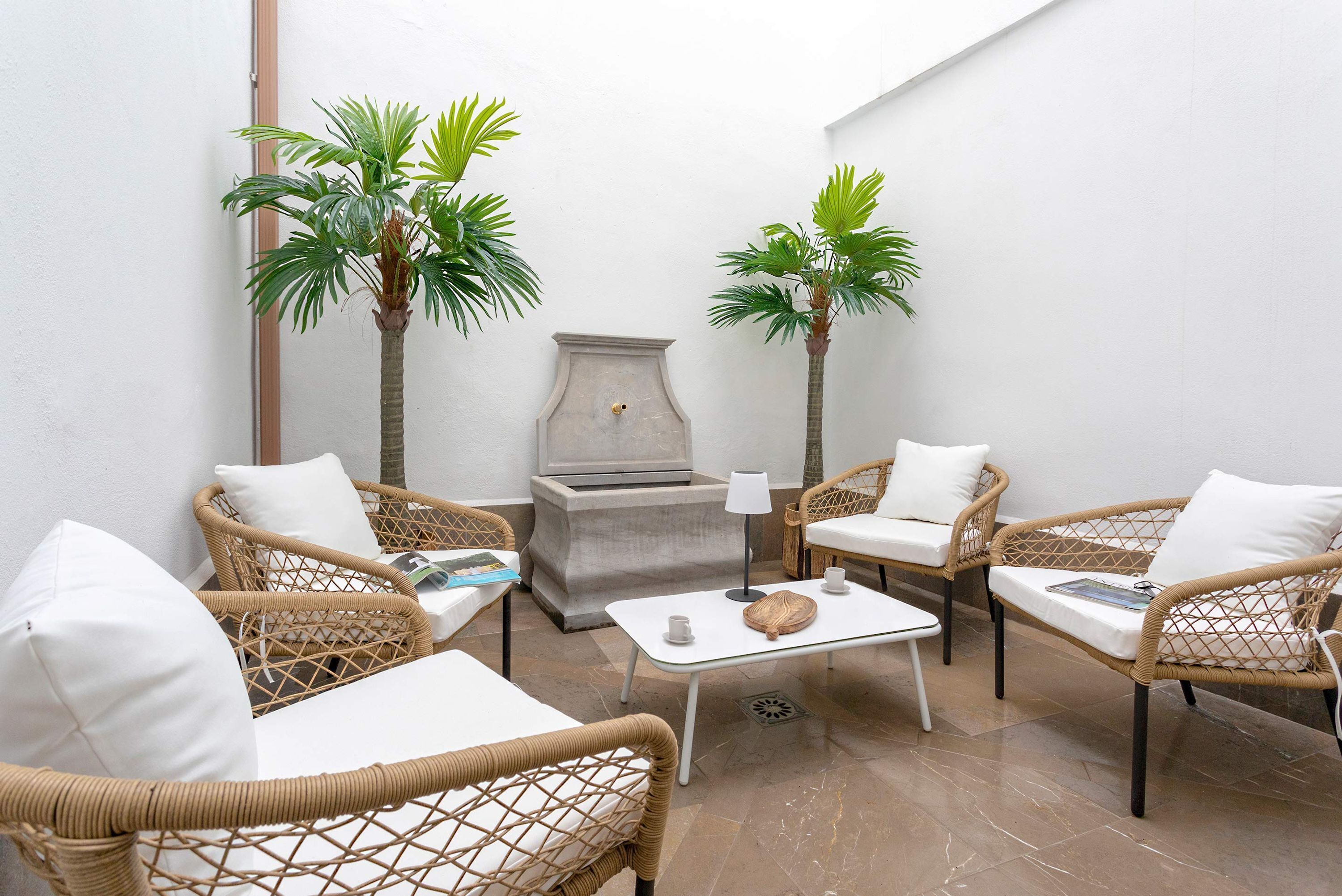A cozy outdoor seating area with wicker furniture, a small table, and two palm trees.