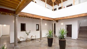 Un ampio cortile con pavimento in pietra, travi in legno e colonne. Si notano piante in vaso e una sedia in vimini.