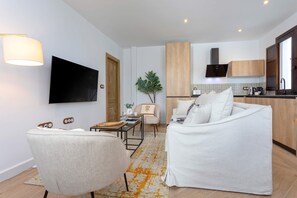 A modern living room with a sofa, armchair, and a flat-screen TV mounted on the wall.