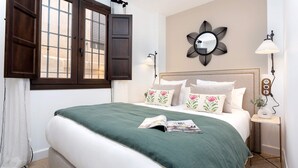 A neatly made bed with a green bedspread and decorative pillows, a wall-mounted mirror, a bedside lamp, and a small table with a plant. - Exclusive Apartment in Granada Horno Marina 11 (Granada)