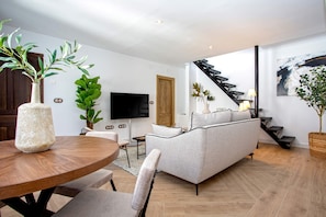 A modern living room with a round wooden table, a grey sofa, and a flat-screen TV. - Exclusive Apartment in Granada Horno Marina 11 (Granada)