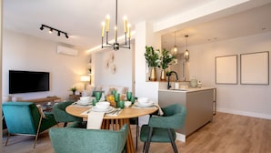 Uma sala de jantar moderna com uma mesa redonda, cadeiras estofadas verdes e um candelabro.