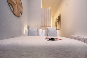 A modern bedroom with a large bed, two pillows, a magazine on the bed, a wooden wall art piece, and a white nightstand. - Luxury Loft in Granada Center La Paz II (Granada)