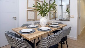 A dining area with a wooden table set for four, surrounded by houndstooth chairs. A white vase with green plants is on the table. - Luxury Apartment in M Laga Victoria (Málaga)