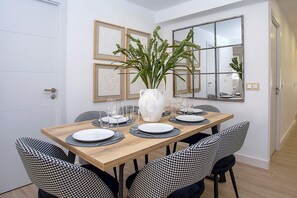 A dining area with a wooden table set for four, surrounded by houndstooth chairs. A white vase with green plants is on the table. - Luxury Apartment in M Laga Victoria (Málaga)