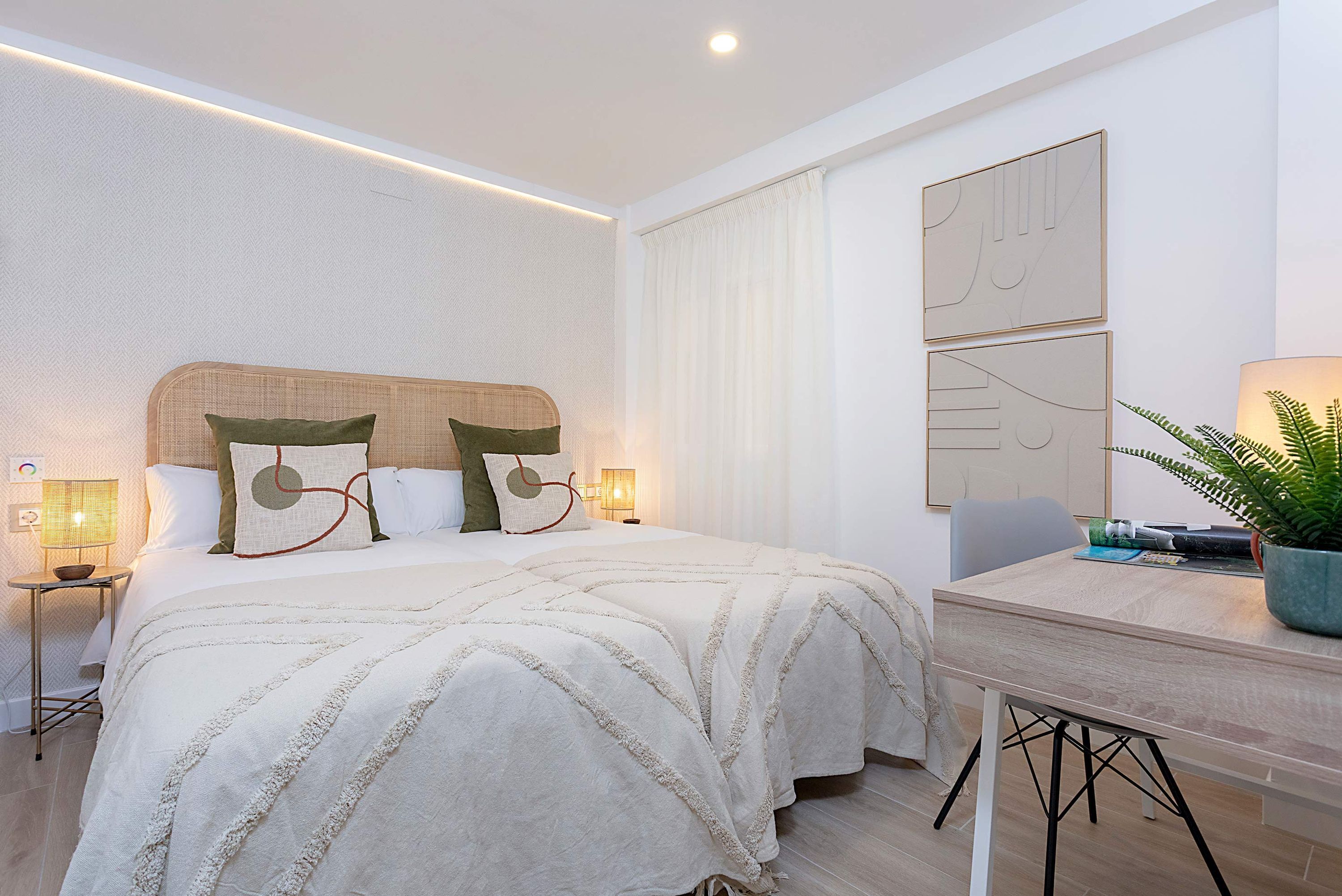 Ein modernes Hotelzimmer mit einem großen Bett, Nachttischen mit Lampen, einem Schreibtisch mit Stuhl und einer Topfpflanze.
