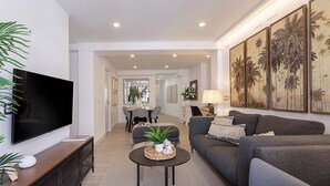 A modern living room with a flat-screen TV, grey sofas, a coffee table, and a dining area in the background. - Luxury Apartment in M Laga Victoria (Málaga)