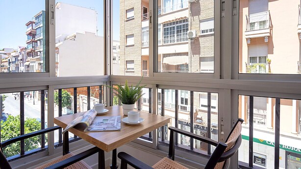 A balcony with a wooden table, two chairs, a potted plant, and a newspaper. - Luxury Apartment in M Laga Victoria (Málaga)
