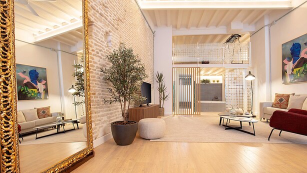 Un salon moderne avec un grand miroir, un plancher en bois, une plante en pot, un canapé, un fauteuil rouge et une table basse.