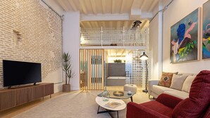 Un salon moderne avec un téléviseur à écran plat, un fauteuil rouge, une table basse et une bibliothèque.