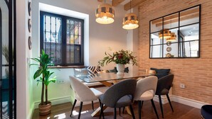 A dining area with a glass table, six chairs, and hanging pendant lights. - Exclusive Sevillian House With Terrace Casa San Lorenzo (Seville)