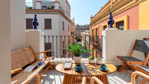 A balcony with a wooden table, chairs, a potted plant, and a view of adjacent buildings. - Exclusive Sevillian House With Terrace Casa San Lorenzo (Seville)