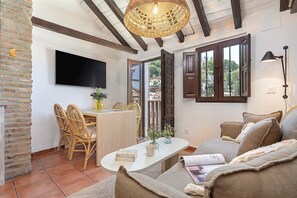 A cozy living room with a white sofa, a dining table with wicker chairs, a flat-screen TV mounted on the wall, and a large window with wooden shutters. - Luxury House in Granada Center Reyes II (Granada)