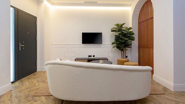 A modern living room with a large sofa, a flat-screen TV mounted on the wall, a small side table, and a potted plant. - Lovely Apartment in Seville Center Lagar I (Seville)