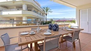 A dining area with a table set for four, outdoor chairs, and a view of a multi-story building with balconies. - Bright Apartment Front of Beach Guadalmansa Beach (Estepona)