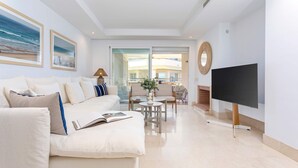 A modern living room with a sofa, a coffee table, and a TV. There is a balcony with a view of buildings. - Bright Apartment Front of Beach Guadalmansa Beach (Estepona)