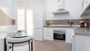 A modern kitchen with white cabinets, a stainless steel range hood, a built-in oven, and a glass dining table with a chair.