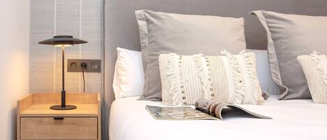 A neatly made bed with a magazine, a lamp, and a wooden nightstand with drawers.