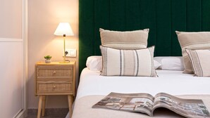 Una cama bien hecha con un cabecero verde oscuro, dos mesitas de noche con lámparas y una revista sobre la cama.