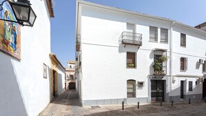 Una estrecha calle adoquinada bordeada por edificios blancos con balcones y un mural a la izquierda.