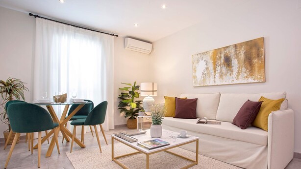 Una sala de estar moderna con un sofá blanco, sillas verdes, una mesa de centro y una zona de comedor con una mesa y sillas.