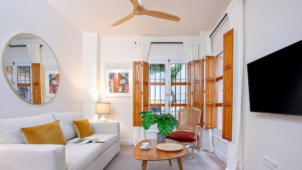 A living room with a white sofa, a round wooden coffee table, a potted plant, a red chair, and a television mounted on the wall. - Bright Apartment in Seville Plaza Santa Cruz (Seville)