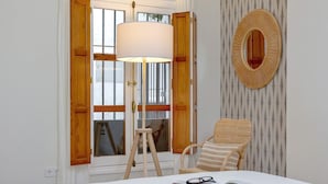 A room with a white bed, a standing lamp, a wicker chair, and a wall-mounted mirror. - Bright Apartment in Seville Plaza Santa Cruz (Seville)