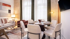 A modern living room with a sofa, chairs, a dining table set for four, and a television mounted on the wall. - Cozy 3BD Duplex in Seville Center Gran Poder II (Seville)