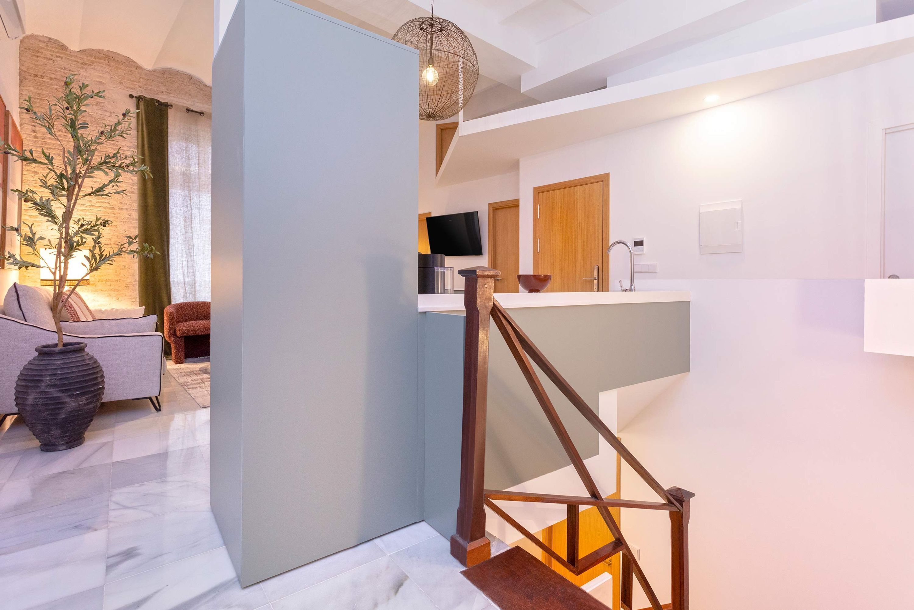 A modern kitchen with a wooden staircase, a dining area with a large vase, and a living room with a sofa and a plant.