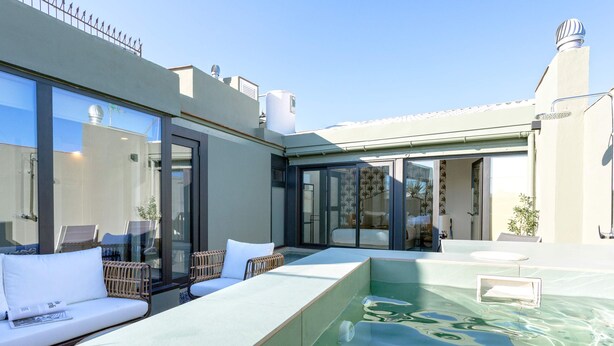 Un espace piscine sur le toit, doté d’une structure en verre, de sièges extérieurs et d’un élément décoratif aquatique.