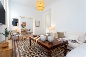 Ein modernes Wohnzimmer mit Couchtisch aus Holz, weißem Sofa und fußbodenhohen, gemusterten Fliesen.
